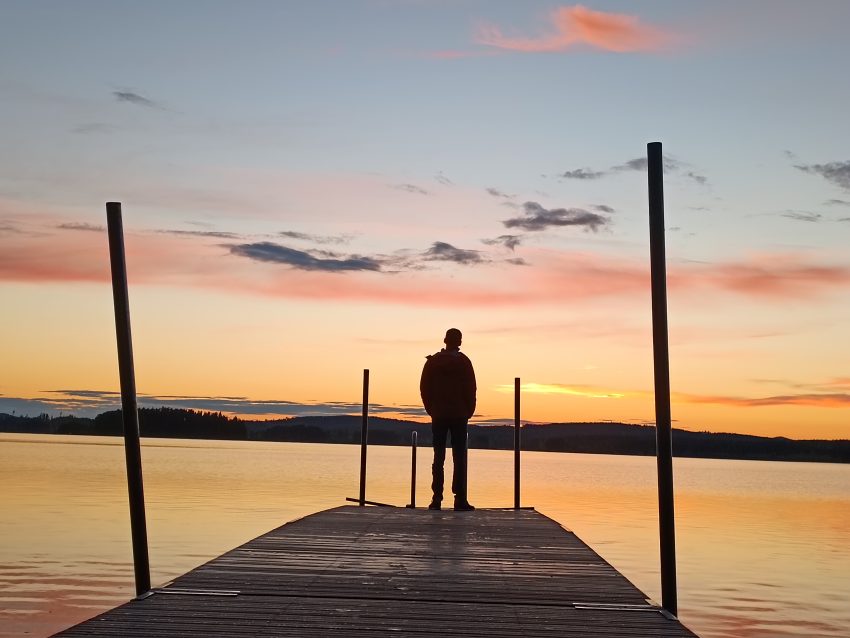 Silhouette of person staning on a jetty with a sunset background