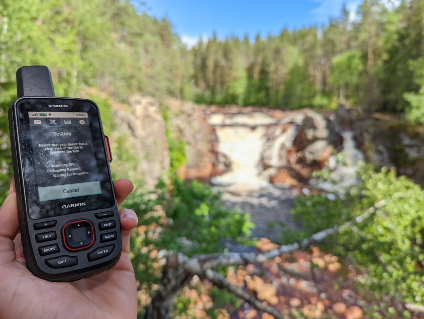 A hand holding a GPS device with a waterfall in the background