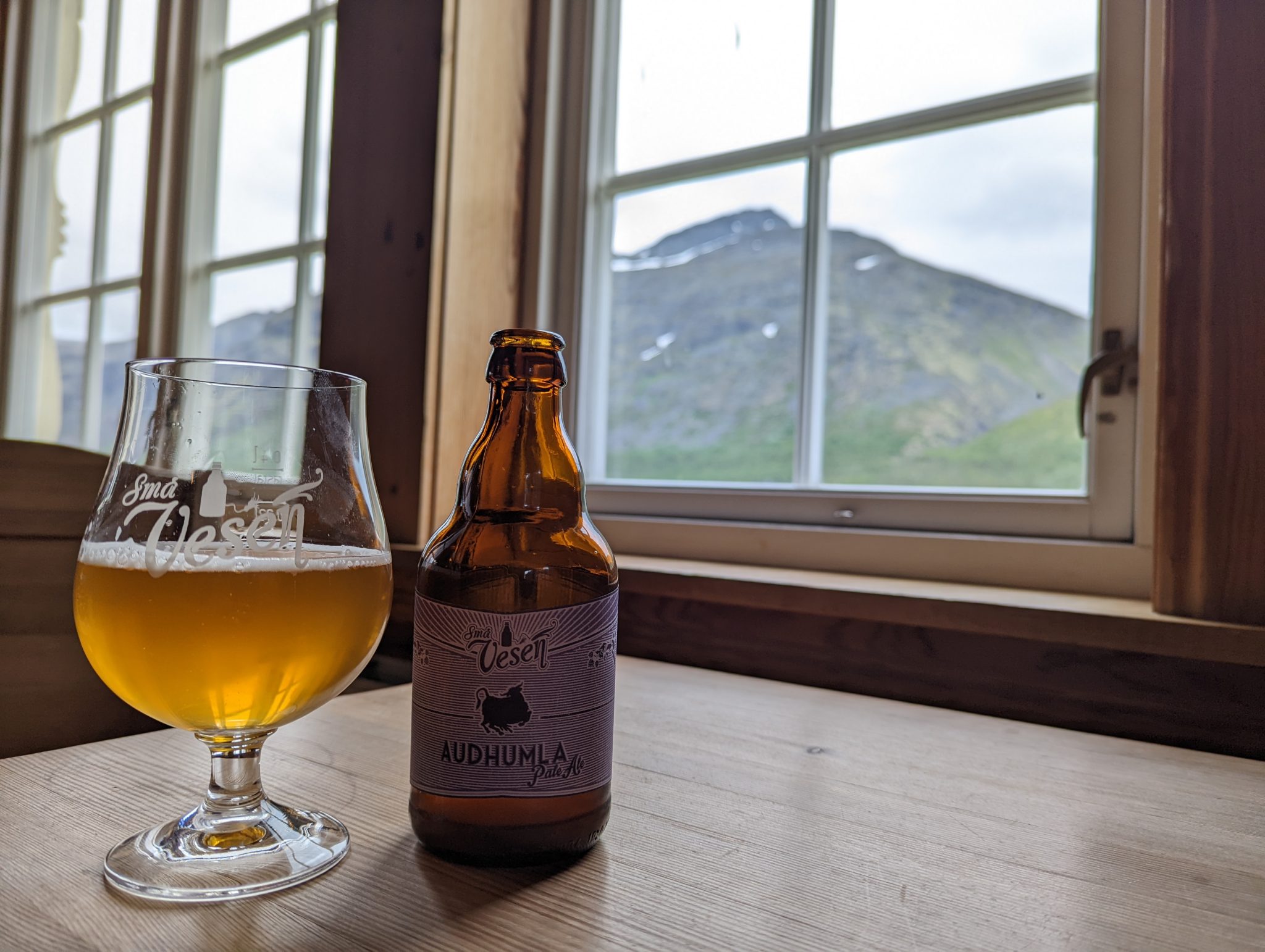 a beer with behind it a cabin window looking at a bare mountain